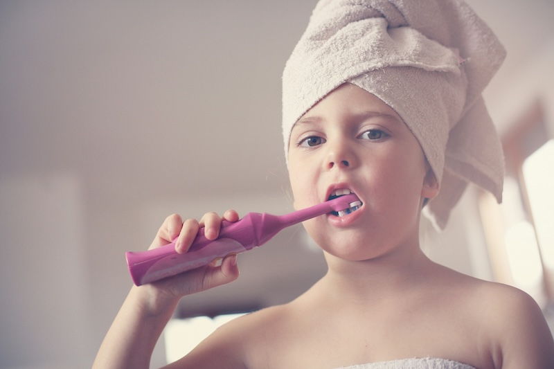 little girl using electric toothbrush to brush her teeth